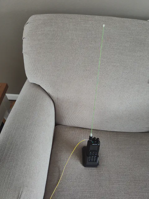 anytone d878uvii front view far away in holder on couch with glow in the dark signal stick attached and yellow signal strand connected black body two control knobs lcd display control buttons numeric keypad