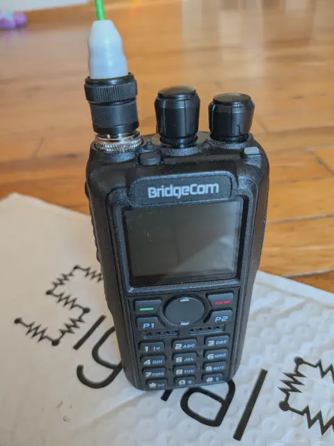 bridgecom maverick front view with green signal stick antenna attached black textured body two control knobs lcd display control buttons numeric keypad